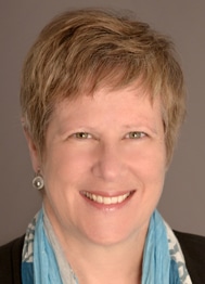 Elise Bean, a woman with short blonde hair wearing a blue scarf.