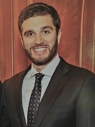 Peter Kenny, a dark haired man wearing a dark suit and dark polka dotted tie.