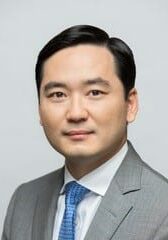 Sang Yi, a dark haired wearing a gray suit and blue tie.