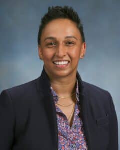 Arya Hariharam, a brown skinned woman with short dark hair wearing a dark jacket and purple shirt.